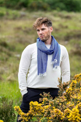 Man wearing McNutt of Donegal blue Oxford scarf in a field with yellow flowers.